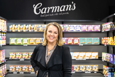 Australian businesswoman and founder of Carman's Fine Foods, standing confidently with arms crossed, smiling in a bright, modern office environment, symbolizing success and entrepreneurship.