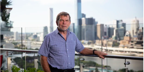 Graham Turner, co-founder of Flight Centre Travel Group, stands in front of a travel agency storefront, representing his impact on the travel industry.