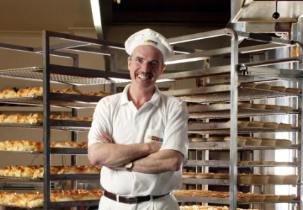 Tom O'Toole, a renowned Australian entrepreneur and inspirational speaker, stands in front of the Beechworth Bakery, showcasing his successful bakery business.