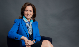 A professional portrait of Debby Blakey, the CEO of HESTA, smiling confidently in a business suit. The background features a modern office setting, highlighting her leadership role in the superannuation industry, advocating for responsible investment and women's financial security.