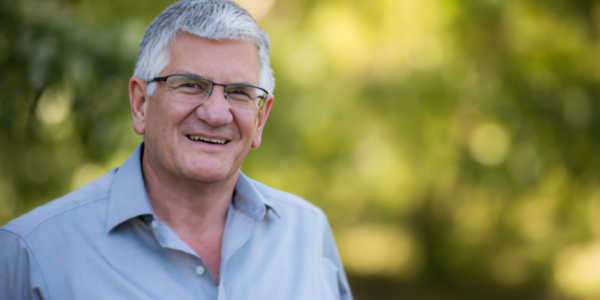 Peter Irvine, co-founder of Gloria Jean’s Coffees, smiling confidently in a business suit.