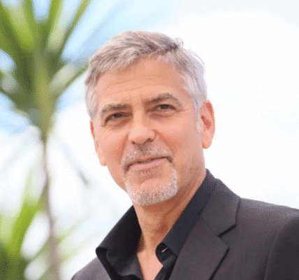 George Clooney smiling at a red carpet event wearing a black tuxedo