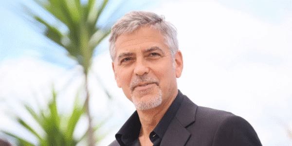 George Clooney smiling at a red carpet event wearing a black tuxedo