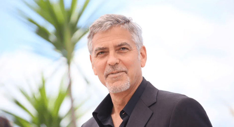 George Clooney smiling at a red carpet event wearing a black tuxedo