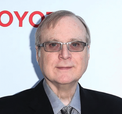 Paul Allen smiling while wearing glasses and a suit jacket at a public event.