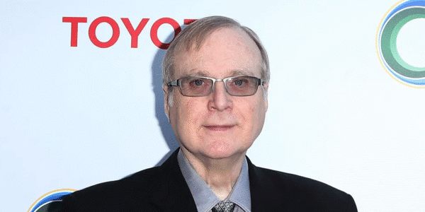 Paul Allen smiling while wearing glasses and a suit jacket at a public event.