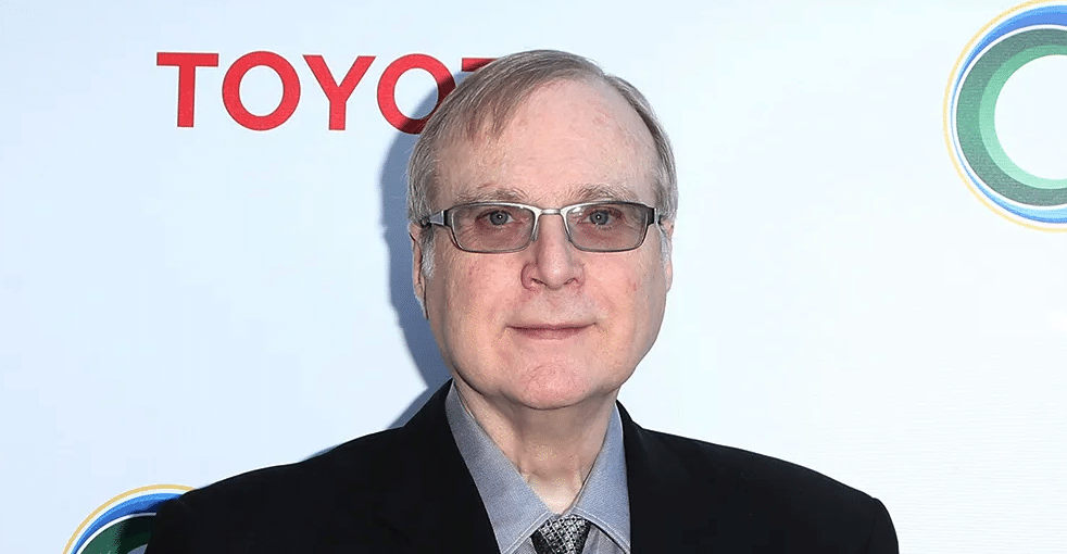 Paul Allen smiling while wearing glasses and a suit jacket at a public event.